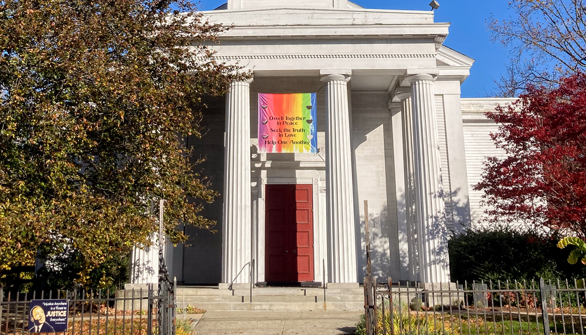 Church portico with tall white columns and a banner saying "Dwell together in peace, Seek the truth in love, and help one another".